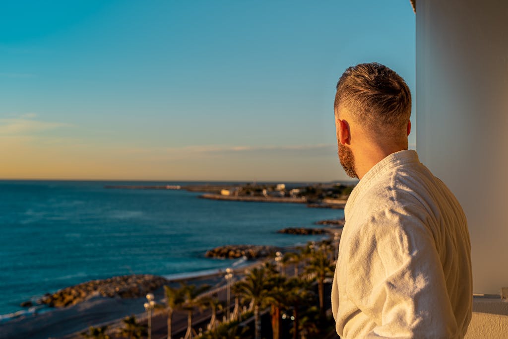 Man in bathrobe enjoys tranquil coastal view from balcony in Nice, France during sunrise.